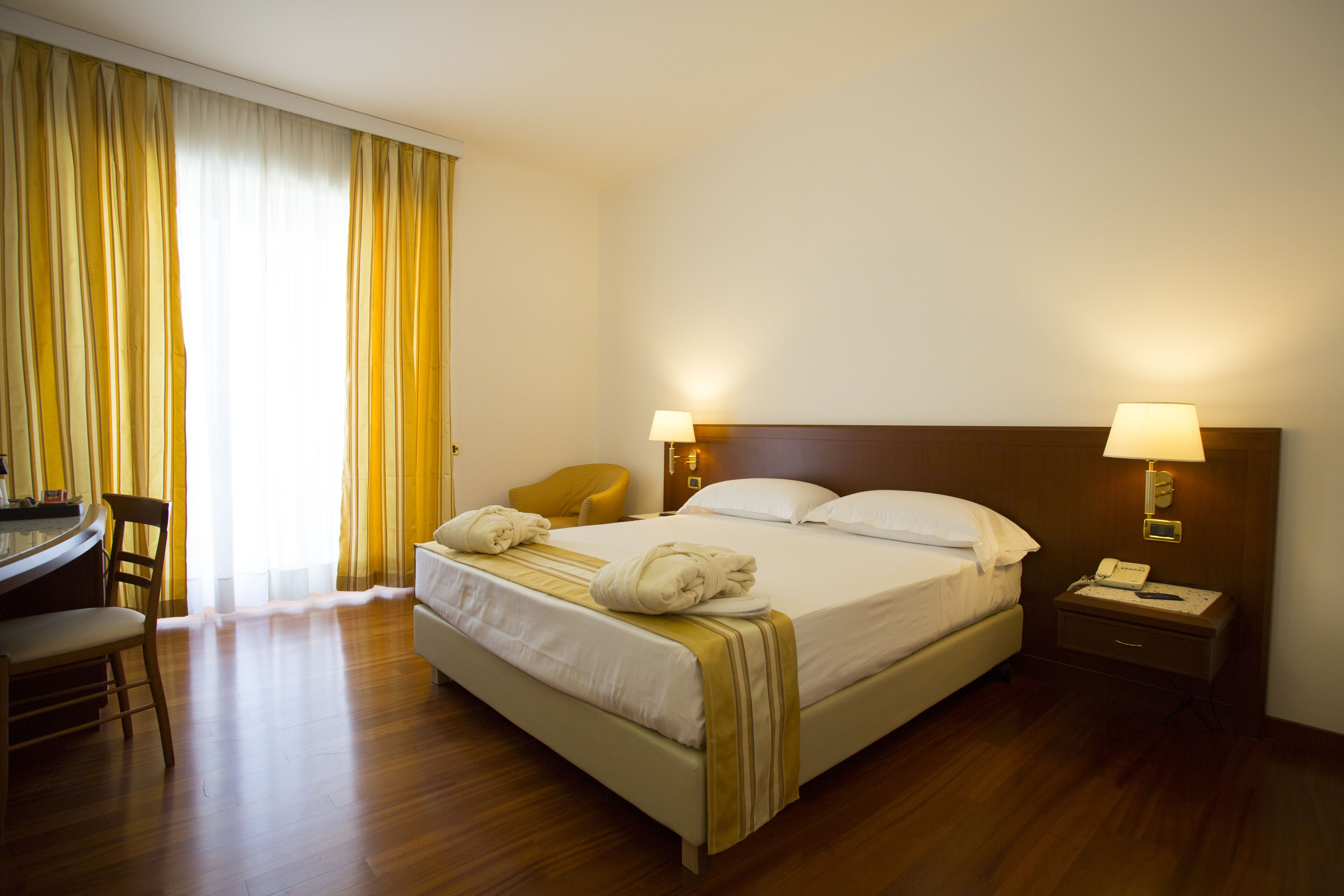 A hotel room with a bed, bedside lamps, a desk, and a chair.