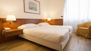 A hotel room with a double bed, bedside lamps, a telephone, a chair, and a painting on the wall.