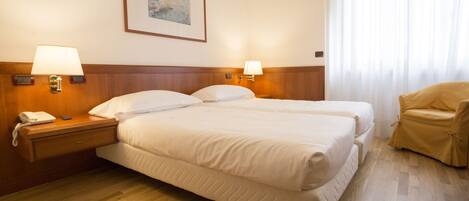 A hotel room with a double bed, bedside lamps, a telephone, a chair, and a painting on the wall.
