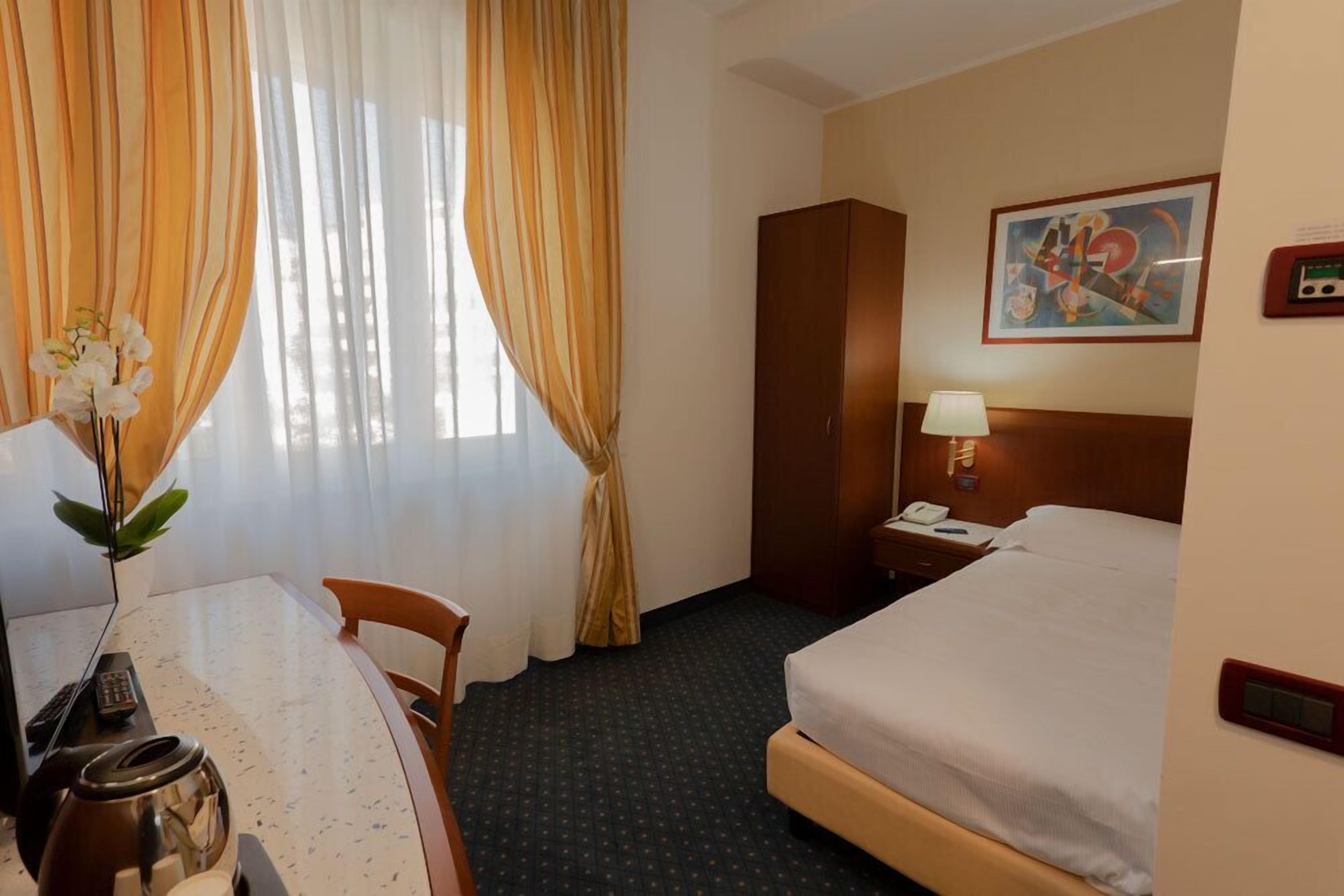 Habitación de hotel con cama, escritorio con lámpara, teléfono y un cuadro en la pared.