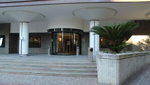 A building entrance with a revolving door, steps leading up to it, and a planter with greenery. - Hotel Europa (Rende)