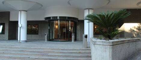 A building entrance with a revolving door, steps leading up to it, and a planter with greenery.