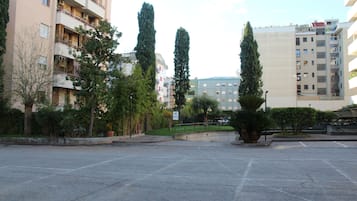 Un aparcamiento con árboles altos y un edificio con balcones al fondo.