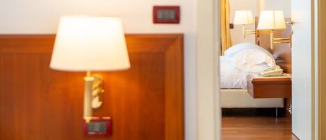 Habitación de hotel con cabecera de madera, lámpara de noche, teléfono y cama con ropa blanca.