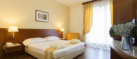 Habitación de hotel con una cama grande, lámparas de noche, mesita de noche, escritorio con un florero y ventana con cortinas.