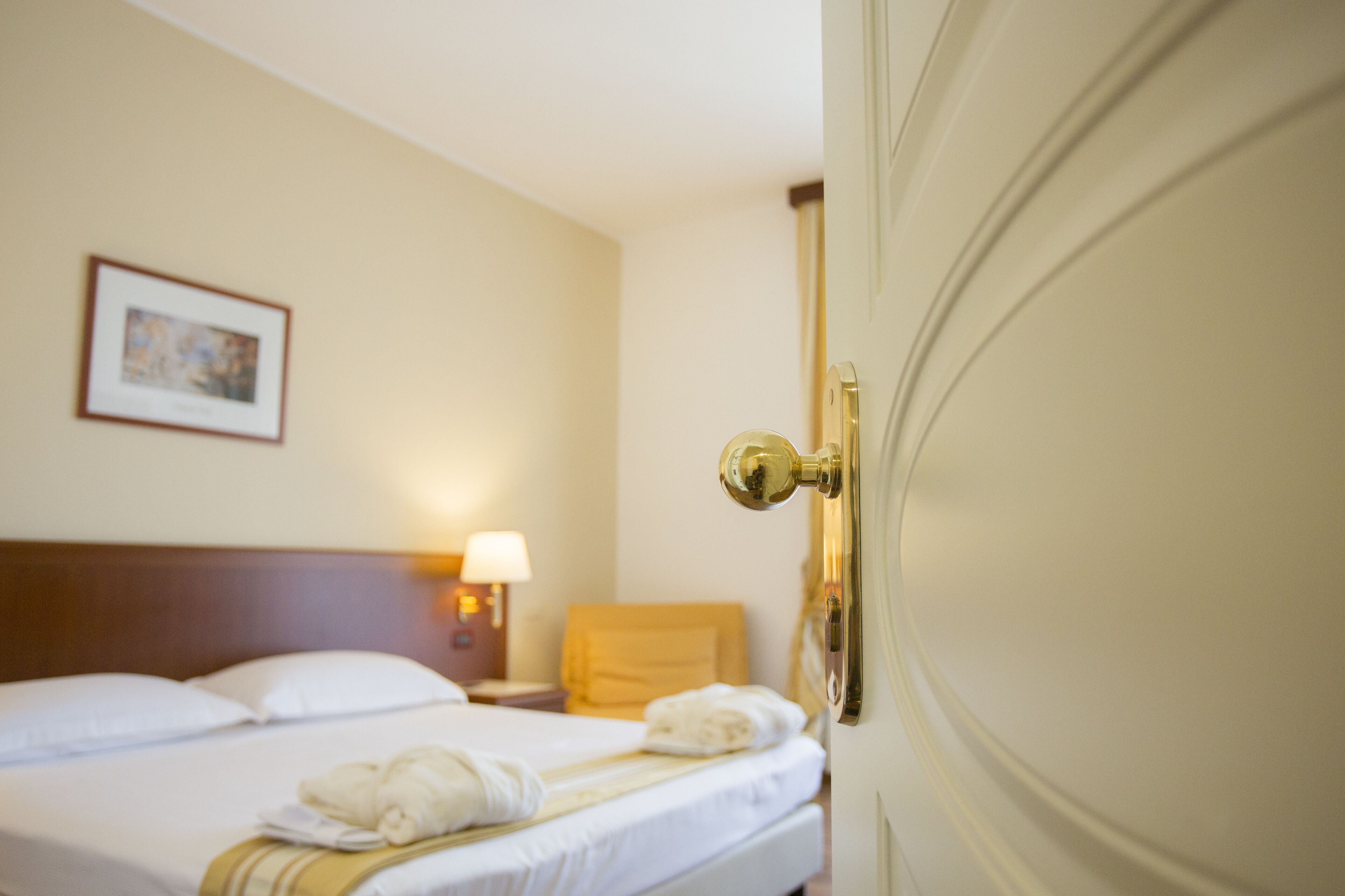 A hotel room with a neatly made bed, a framed picture on the wall, and a lamp on the nightstand.