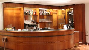 A bar area with wooden cabinets, shelves with bottles, glasses, and a coffee machine. - Hotel Europa (Rende)