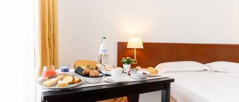 Una mesa de desayuno ordenada con diversos alimentos, una botella y tazas en una habitación de hotel.