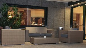 A modern outdoor seating area with wicker furniture, a large potted plant, and a glass wall reflecting the interior. - Hotel Europa (Rende)