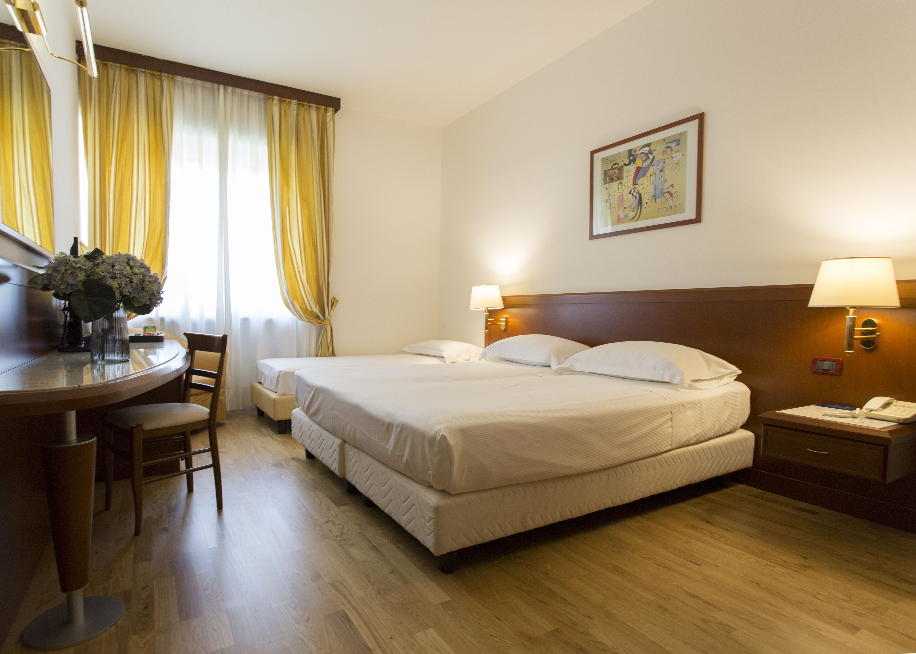Een hotelkamer met twee bedden, een bureau met stoel, een eettafel en een schilderij aan de muur.