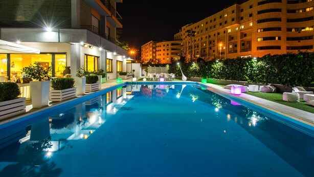 A nighttime swimming pool area with a modern building in the background. - Hotel Europa (Rende)