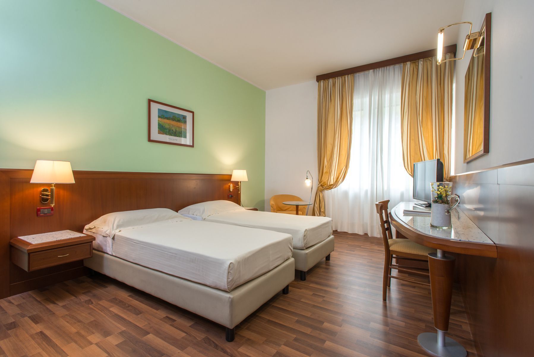 A hotel room with two beds, a desk, a chair, a lamp, a clock, and a framed picture on the wall.