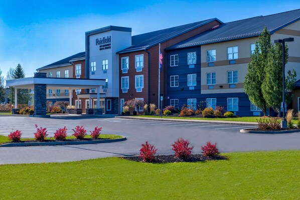 A multi-story hotel with a modern design, featuring a prominent entrance, landscaped gardens, and a parking area.