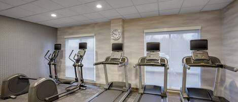 Un gimnasio con cintas de correr, elípticas y una bicicleta estática.