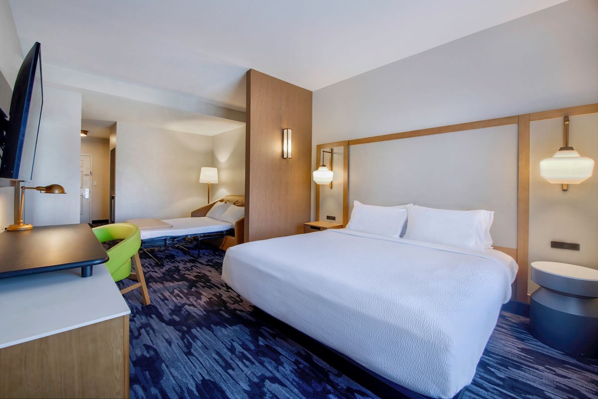 A hotel room with a large bed, a desk with a chair, a television, and a bathroom area.