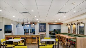 Een modern restaurant met een bar in het midden, gele stoelen en een groen zitgedeelte met banken.