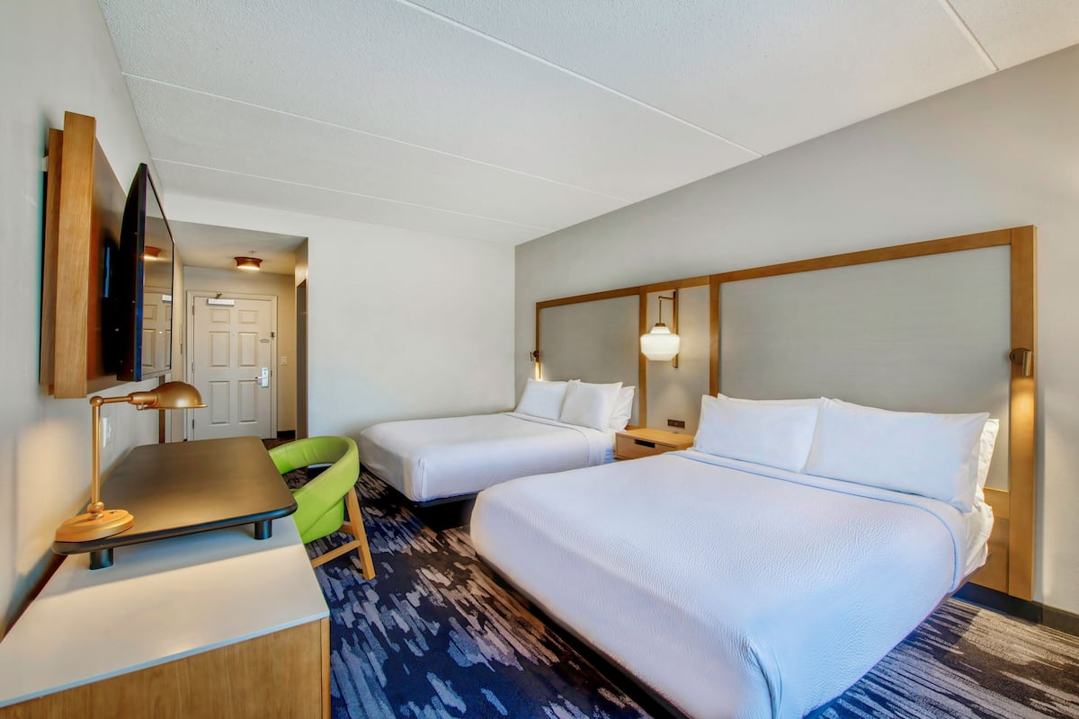 A hotel room with two single beds, a desk with a lamp, a chair, and a large mirror.