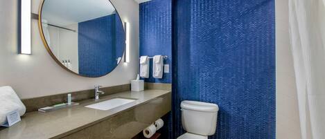 A modern bathroom with a large mirror, two sinks, a toilet, and a shower area.