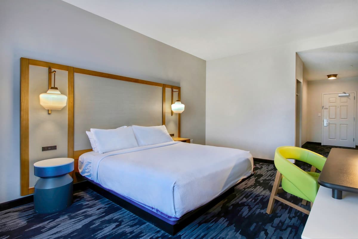 A modern hotel room with a large bed, two bedside tables, a chair, and a desk.