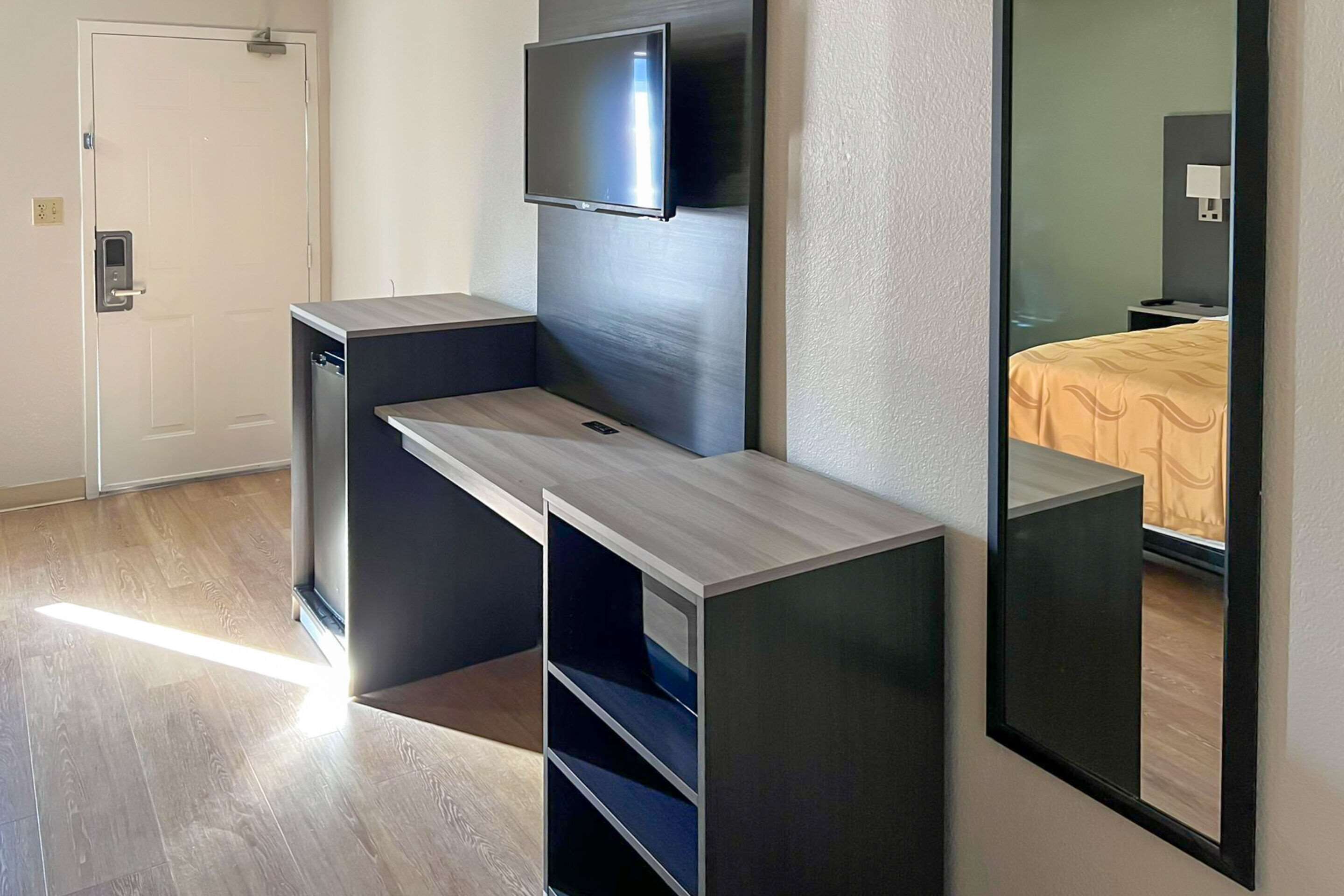 Una camera d'albergo moderna con scrivania integrata, TV a schermo piatto montata a parete e un letto con copripiumino fantasia.