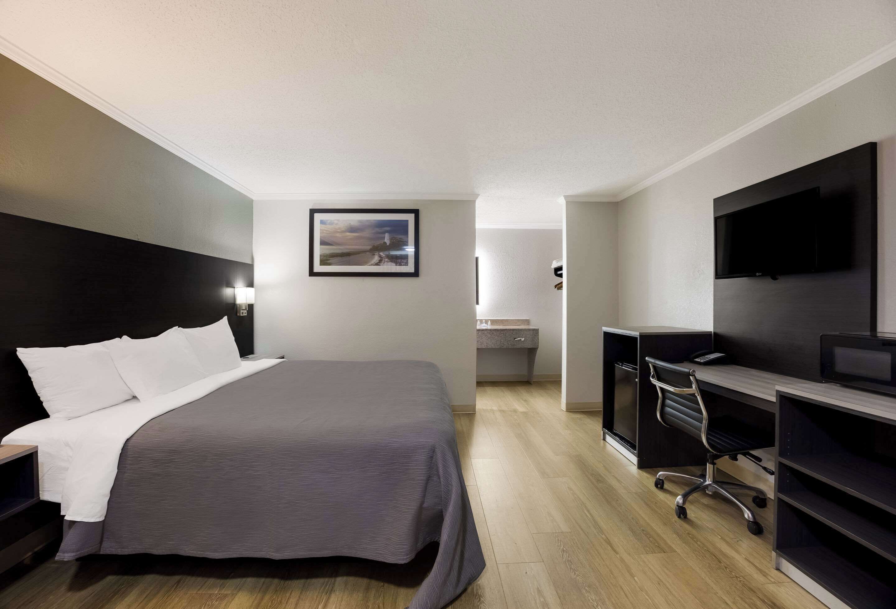 A hotel room with a large bed, a desk, a chair, a TV, and a painting on the wall.
