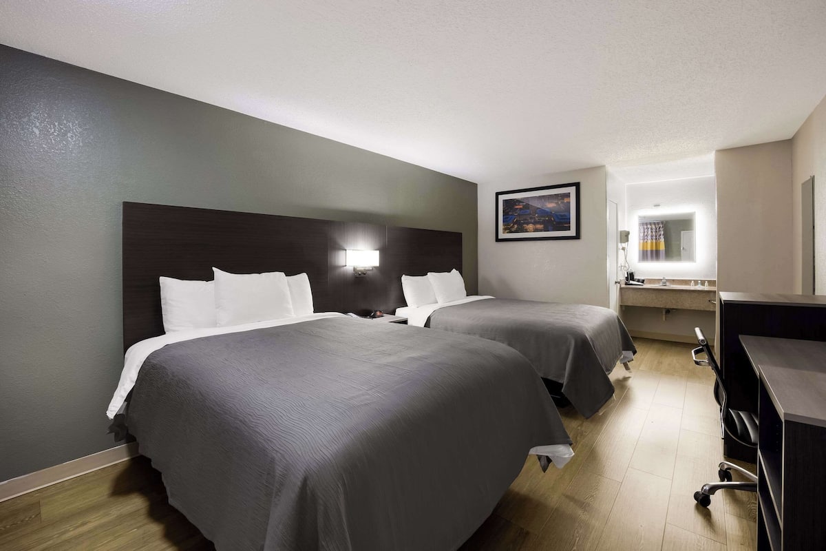 A hotel room with two beds, a desk, and a bathroom.