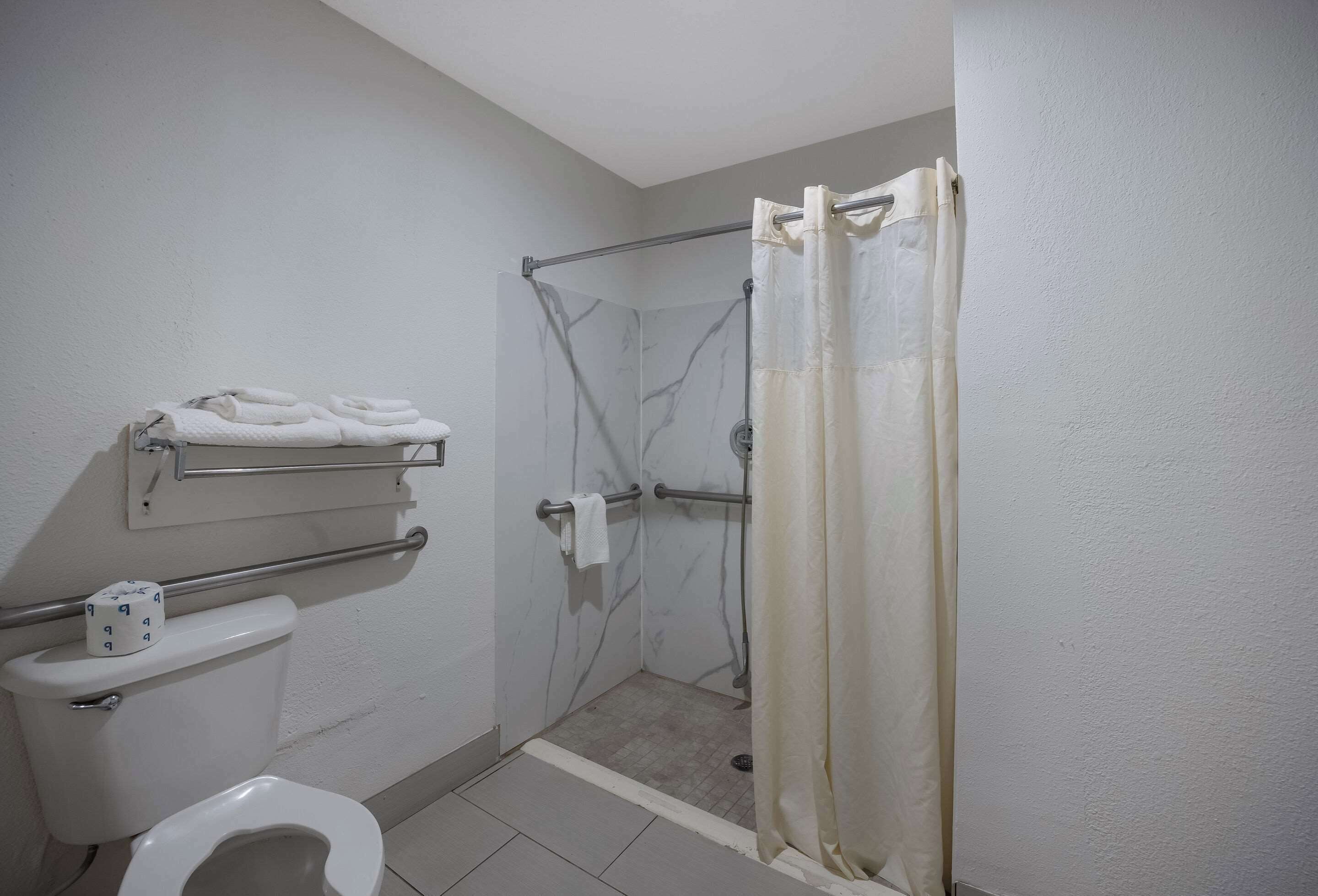 A small bathroom with a toilet, a shower with a grab bar, and a towel rack with towels.