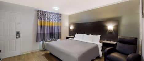 A hotel room with a bed, a chair, a nightstand, and a window with curtains.