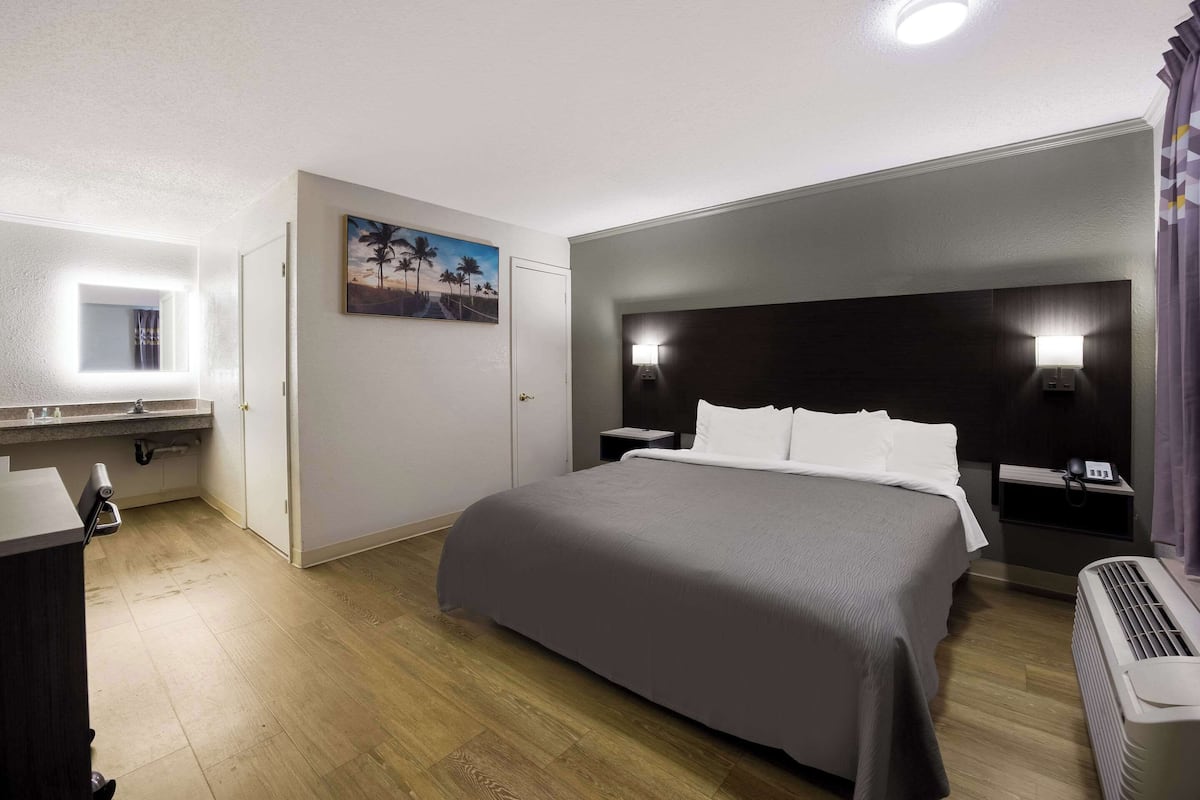 A hotel room with a bed, bedside lamps, a painting on the wall, and a ceiling light.