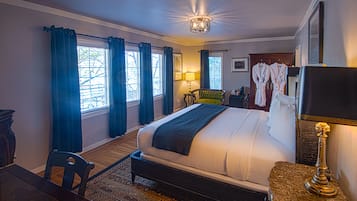 A hotel room with a large bed, a desk, a chair, a lamp, and a wardrobe.
