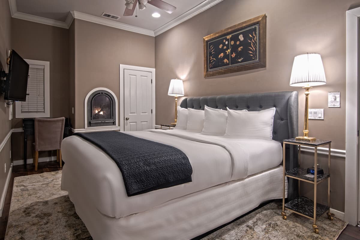 A bedroom with a large bed, two bedside lamps, a fireplace, and a television on the wall.