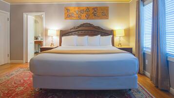 A large bed with a wooden headboard, two bedside tables with lamps, a red patterned rug, and a painting above the bed.