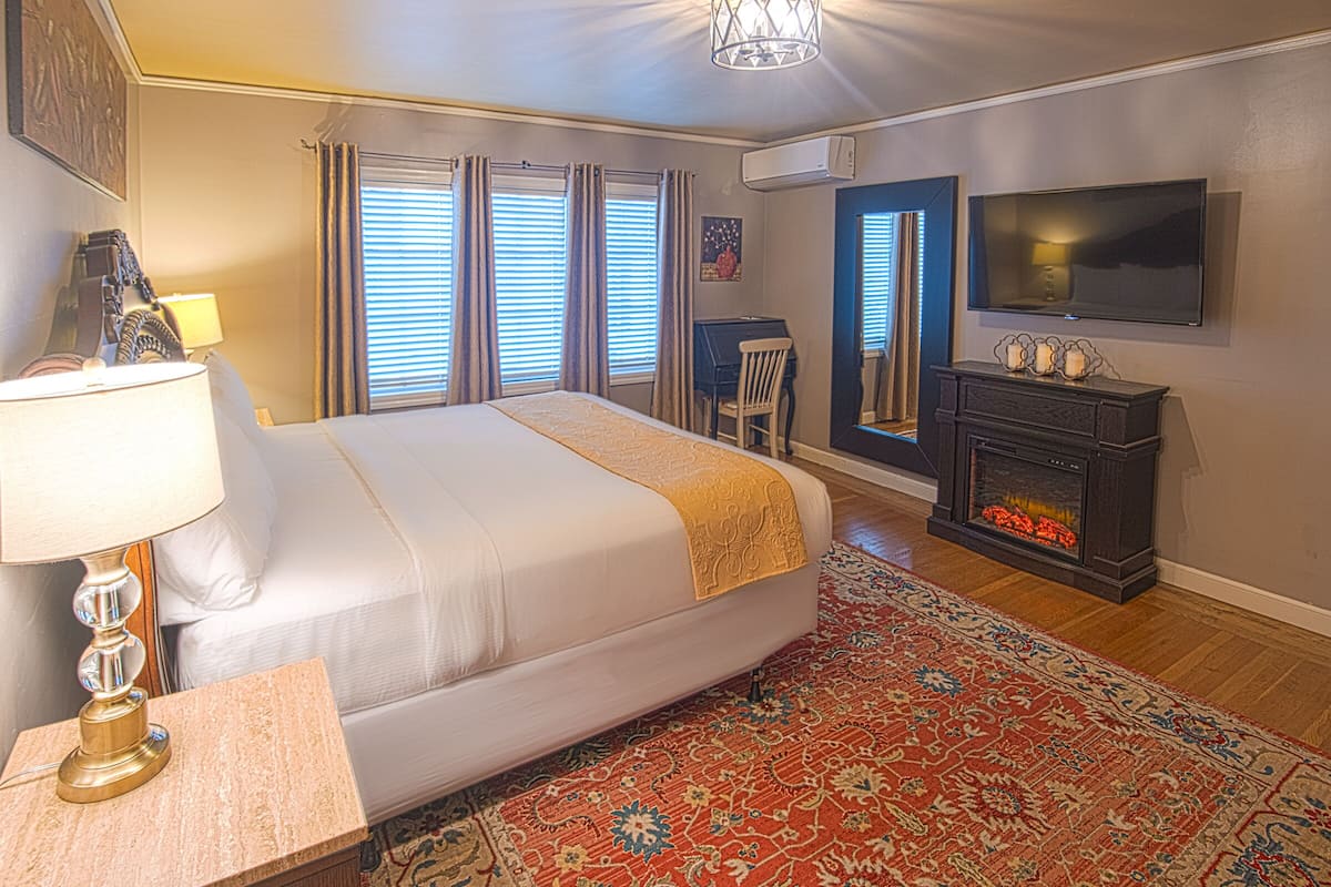 A hotel room with a large bed, a television, a fireplace, and a desk with a lamp.