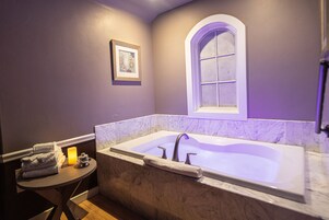 Un baño con una bañera grande, una mesita con toallas, un cuadro en la pared y un ventanal de arco.