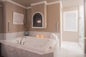 A bathroom with a large bathtub, a fireplace, and a shower area.