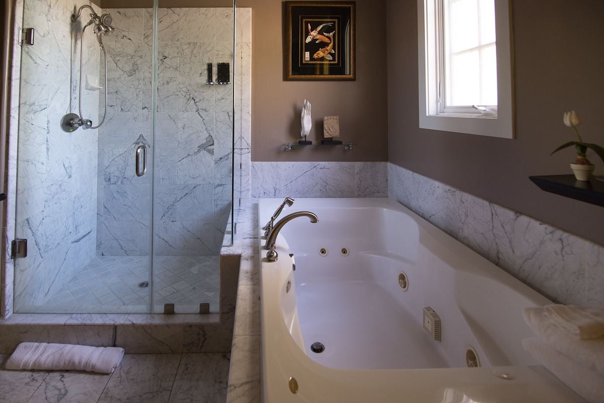 A bathroom with a walk-in shower, a freestanding bathtub, marble walls, and a framed artwork on the wall.