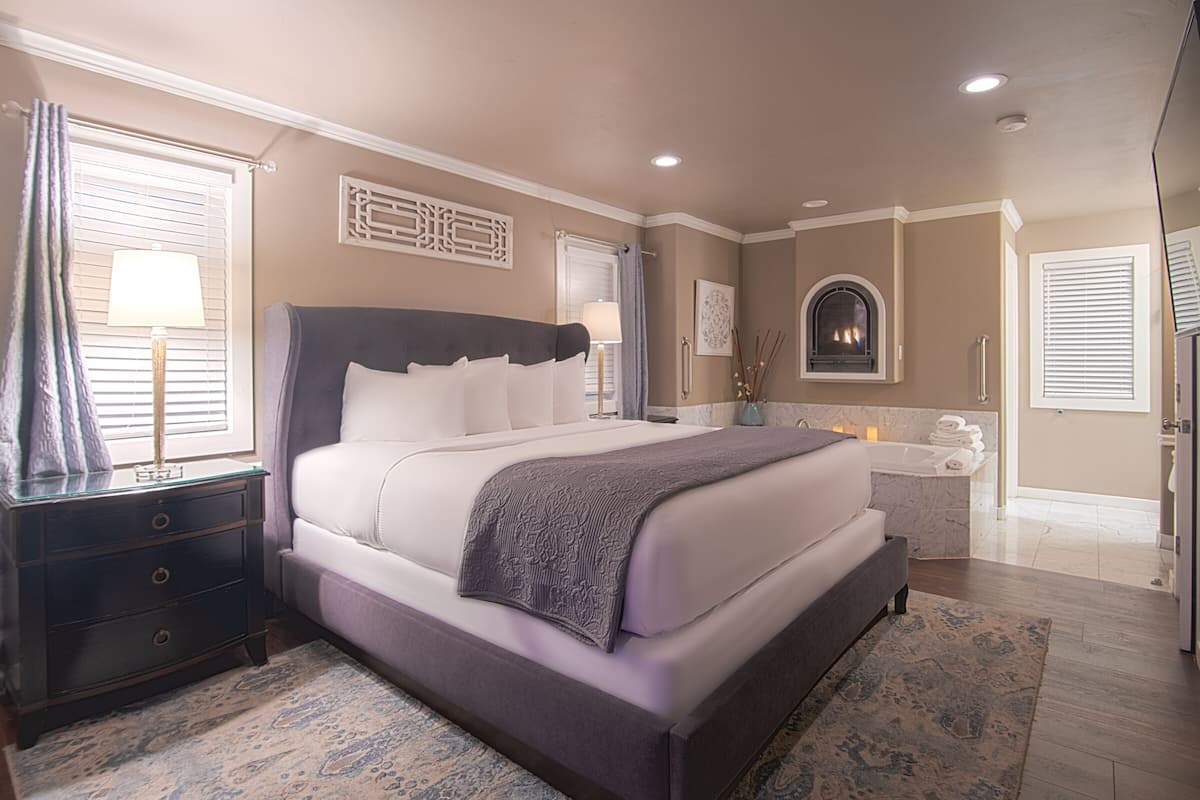 A bedroom with a large bed, a nightstand, a bathroom with a bathtub, and a fireplace.