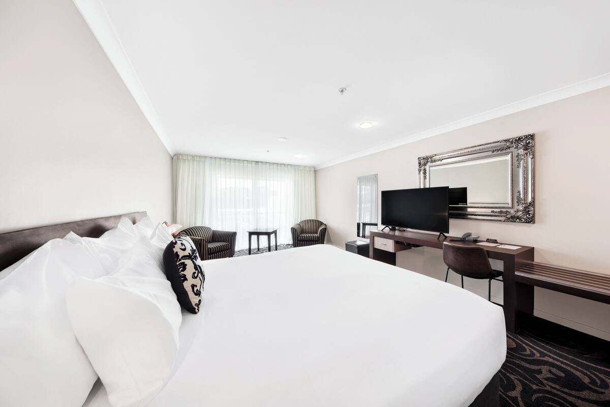 Una habitación de hotel con una cama grande, un escritorio, un televisor y un espejo.