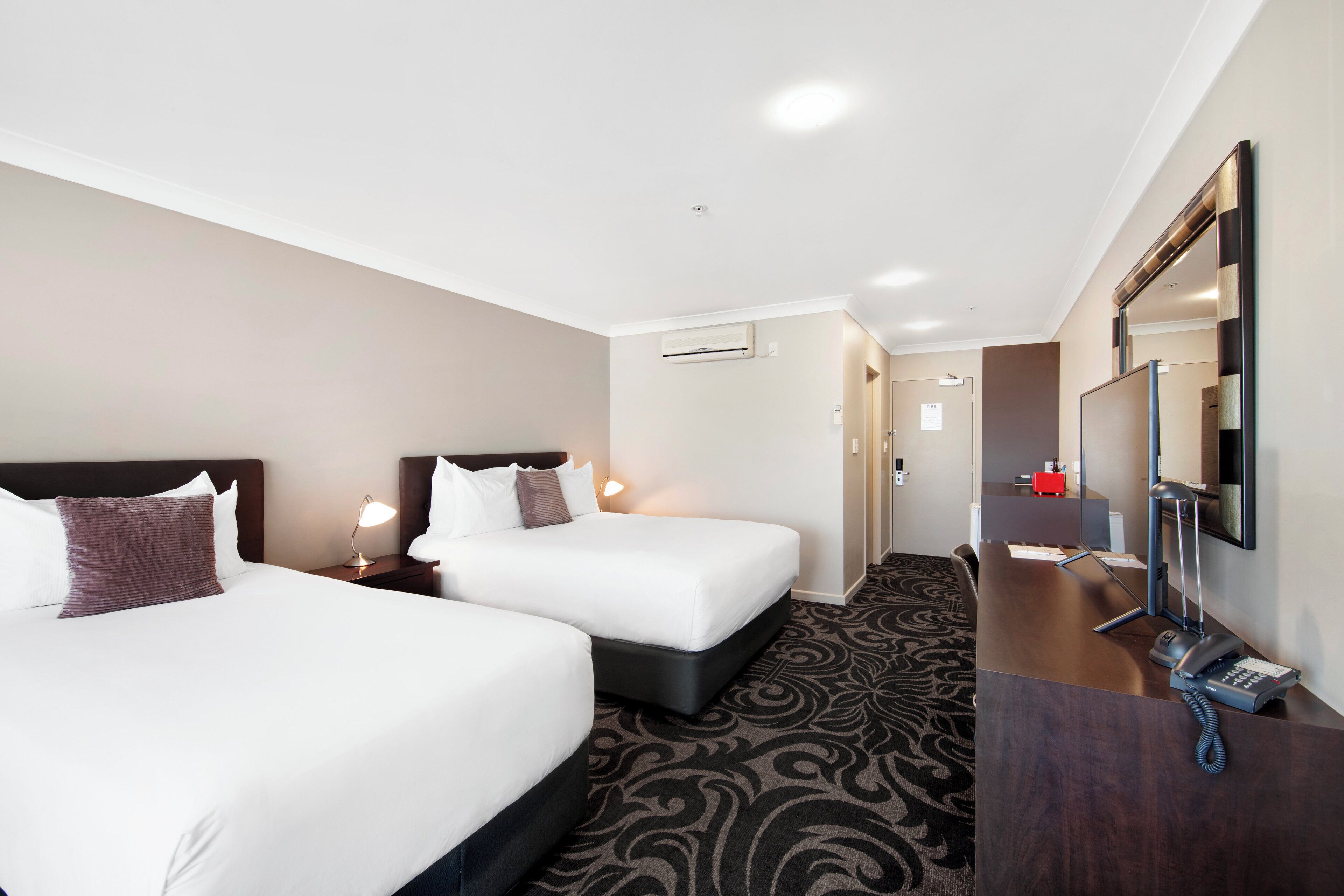 A hotel room with two beds, a desk with a telephone, and a mirror.
