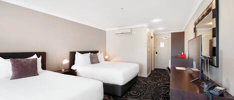 A hotel room with two beds, a desk with a telephone, and a mirror.