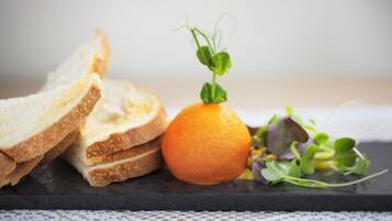 A black slate serving board with slices of bread, an orange, and a small bunch of greens.