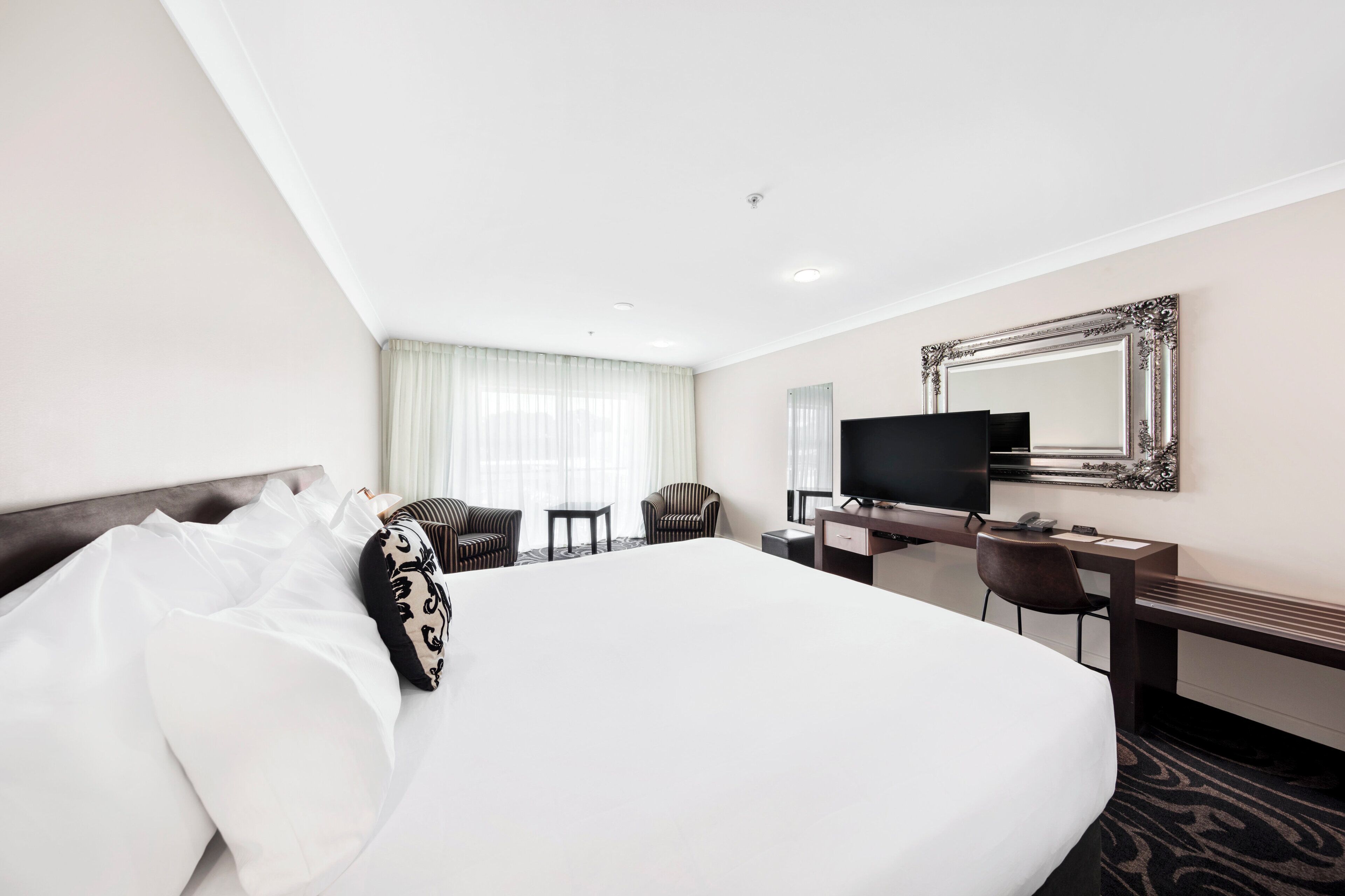Quarto de hotel com uma cama grande, uma escrivaninha com computador, televisão e um espelho na parede.