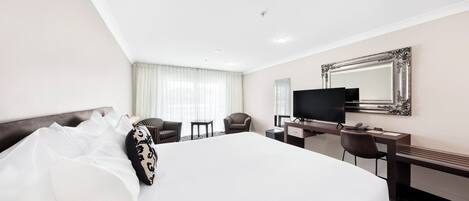 Quarto de hotel com uma cama grande, uma escrivaninha com computador, televisão e um espelho na parede.