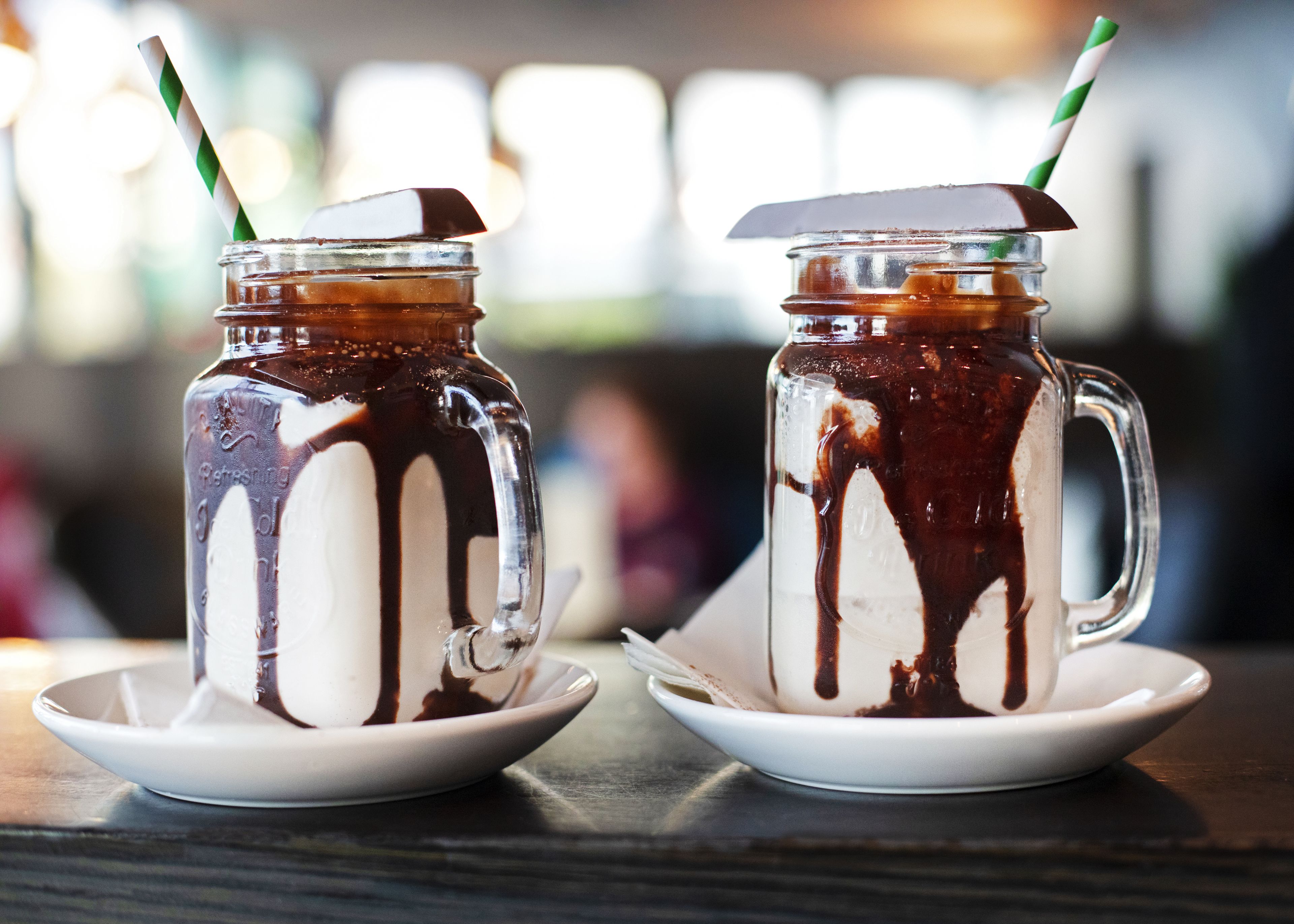 Two iced drinks in mason jars with chocolate drizzles on white saucers.