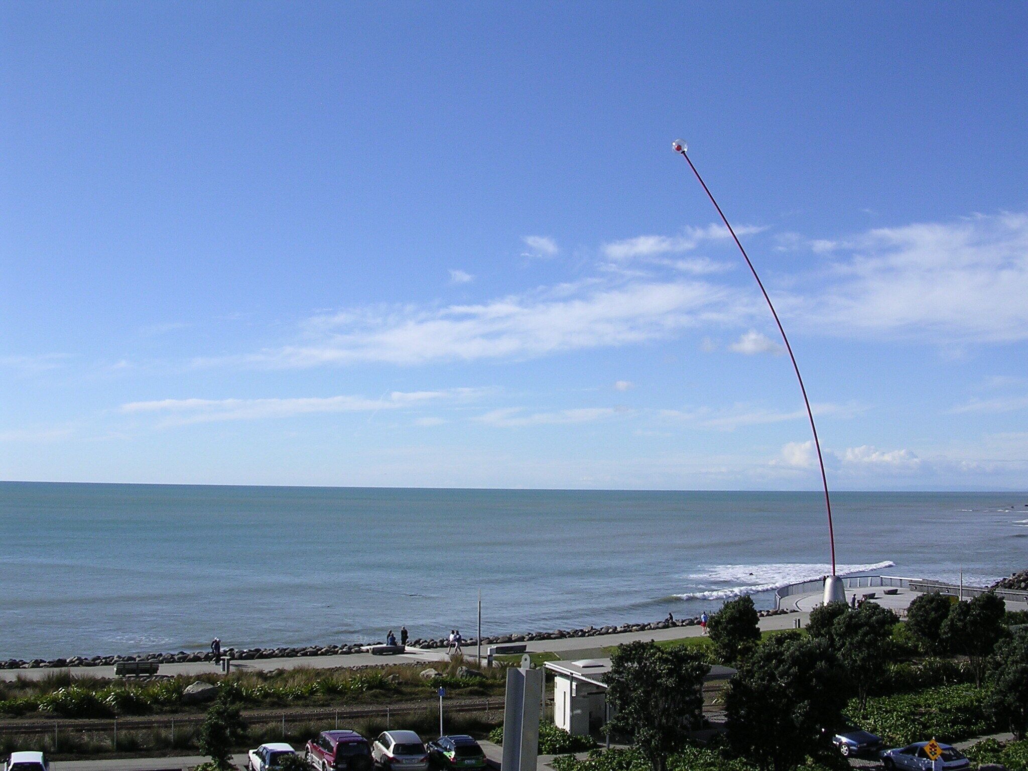 A coastal view with a clear sky, a road with parked cars, and a beach in the distance.