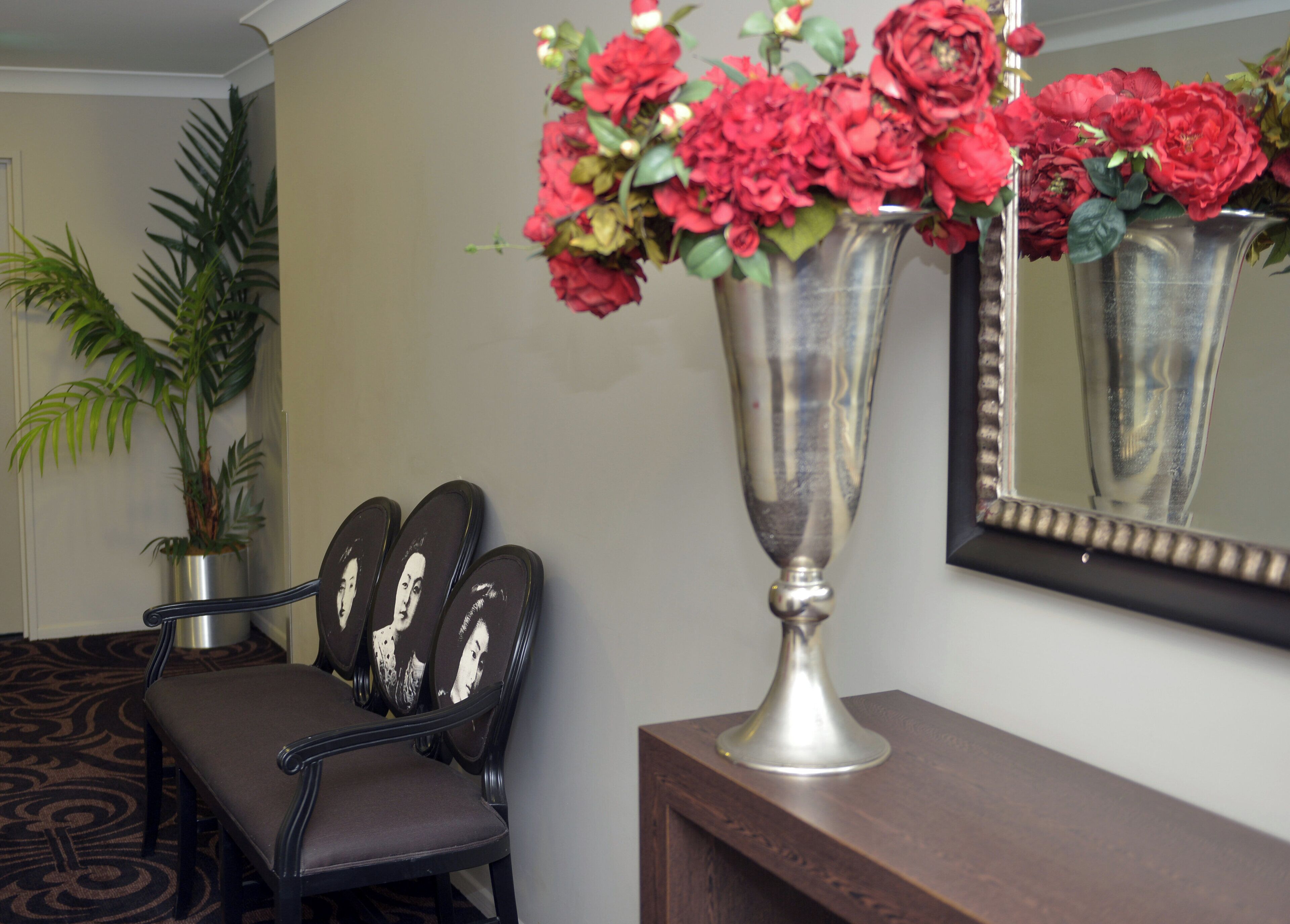 A lobby with a reception desk, a chair with a mirror, and a potted plant.