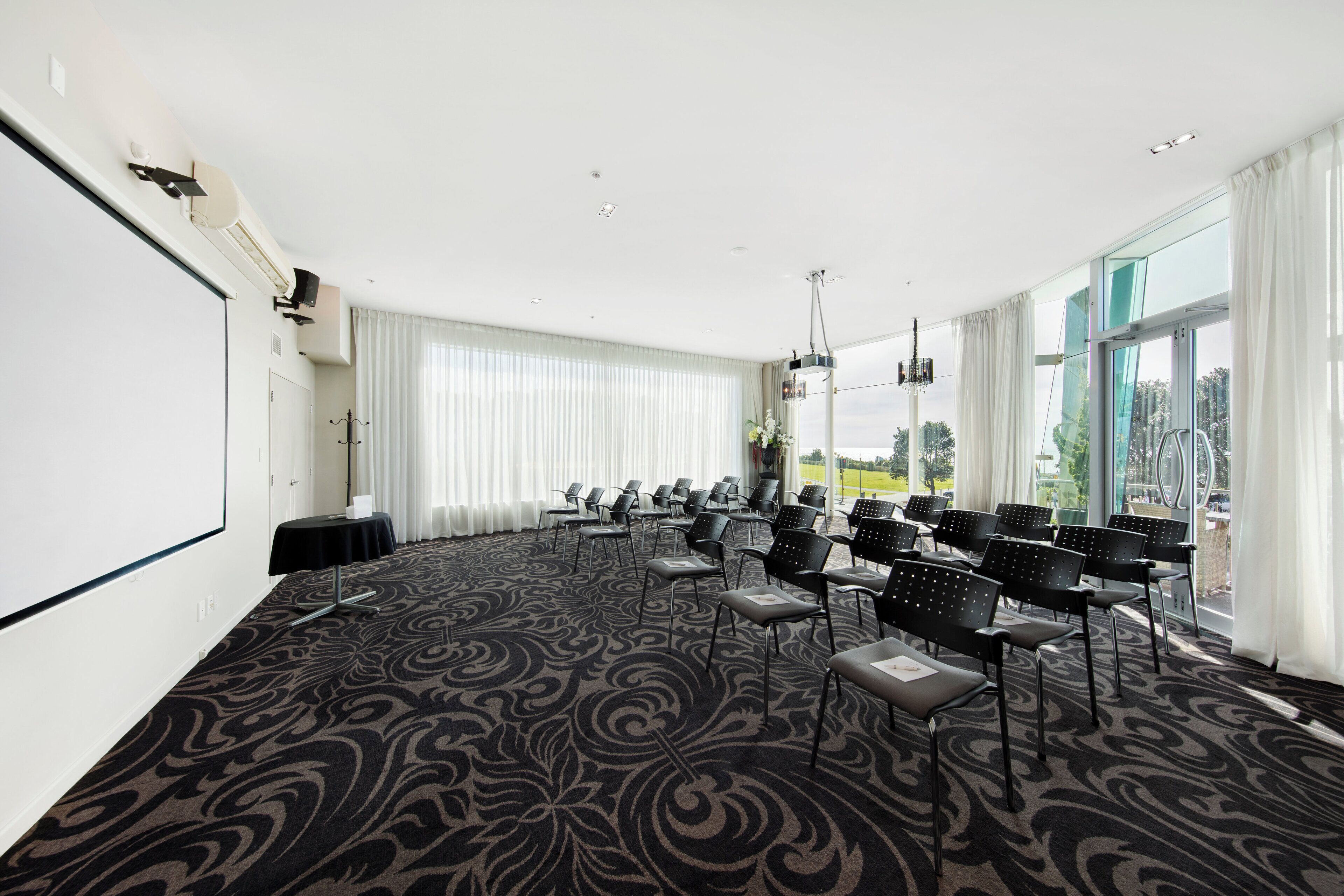 A conference room with a large screen, rows of chairs, and a carpeted floor.
