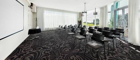 A conference room with a large screen, rows of chairs, and a carpeted floor.