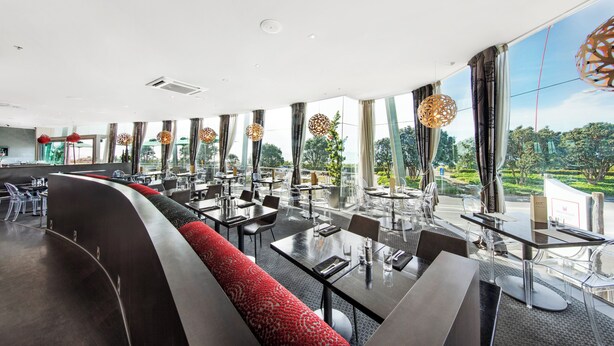 Ein modernes Restaurant mit einer langen Theke, klaren Stühlen und einer rot gemusterten Bank.