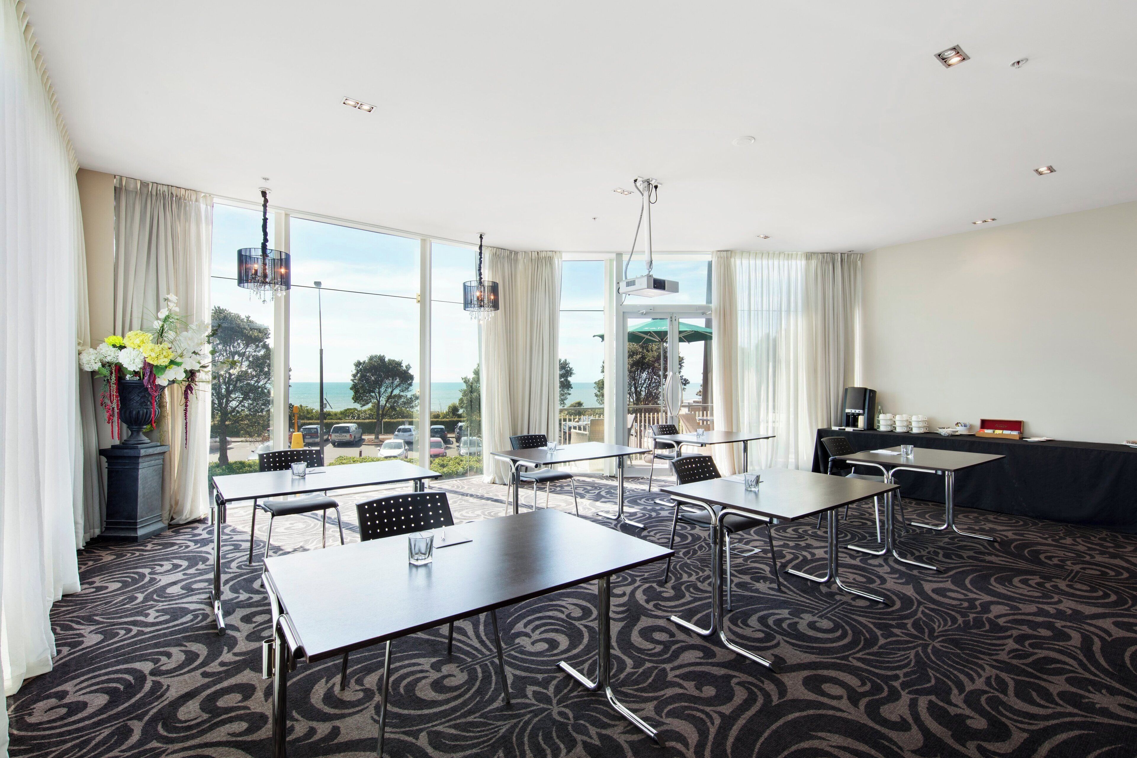 A conference room with tables and chairs, large windows with curtains, a chandelier, and a view of the outdoors.